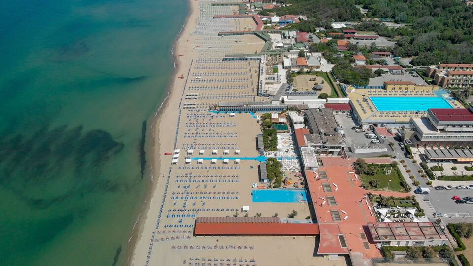 An aerial view of a beach with rows of sun loungers and a swimming pool.