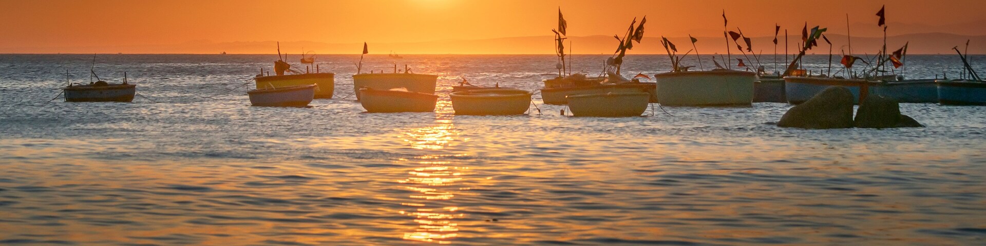 Un atardecer sobre un mar tranquilo con varias embarcaciones ancladas.
