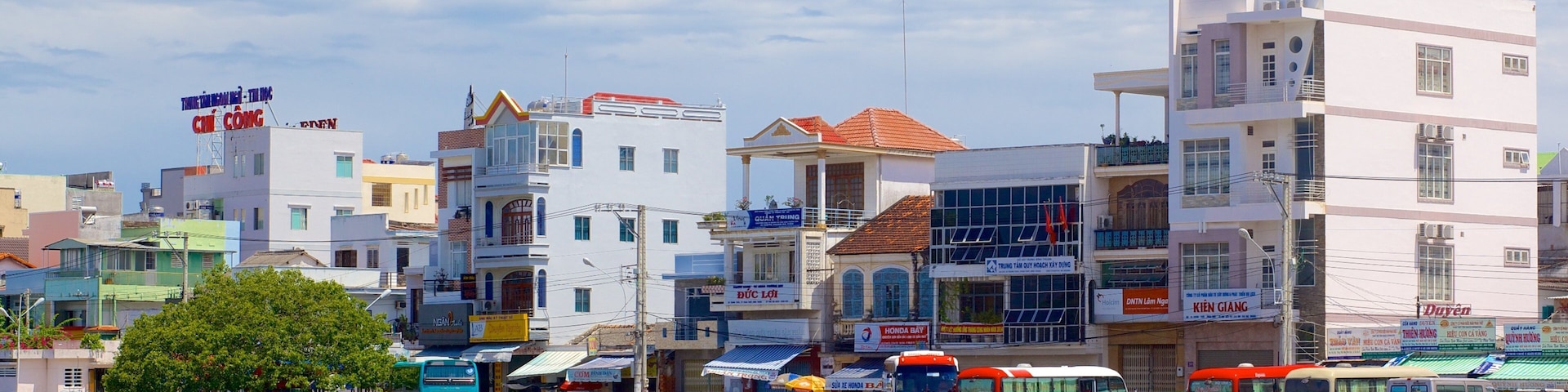 A riverside cityscape with various buildings, including a white building with a red roof and a blue sign.
