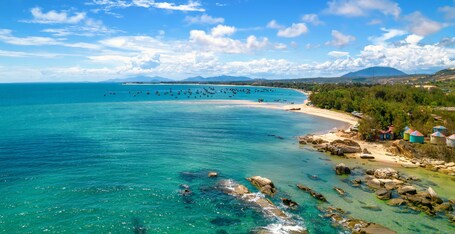Eine Küstenlandschaft mit klarem türkisblauem Wasser, einem Sandstrand und einer Gruppe farbenfroher Gebäude in der Nähe des Ufers.