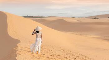Female in white traditional Vietnamese gown and conical hat walking on the beautiful sand dunes of Mui Ne on sunset with copy space, journey, travel, adventure concepts, Mui Ne, Vietnam