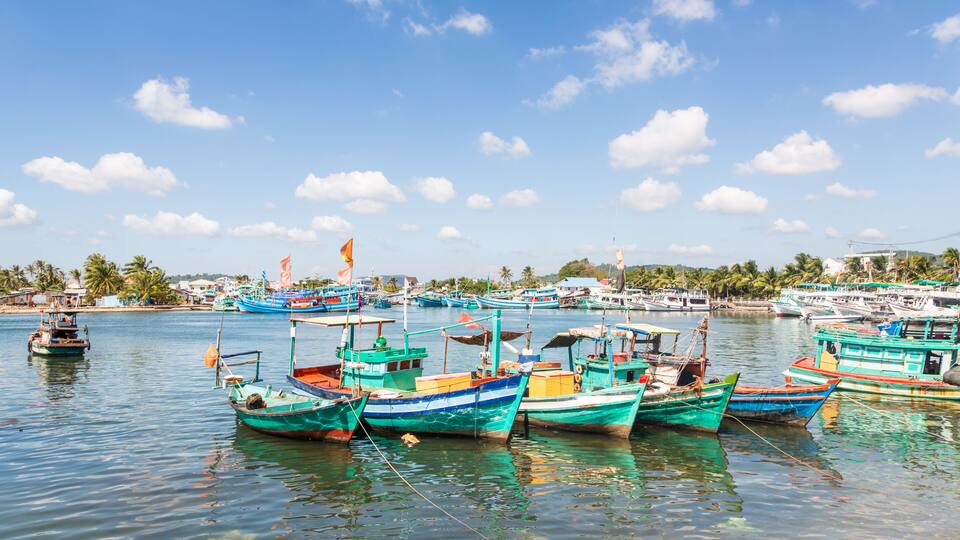 A harbor with colorful boats docked, calm water, and a clear blue sky.