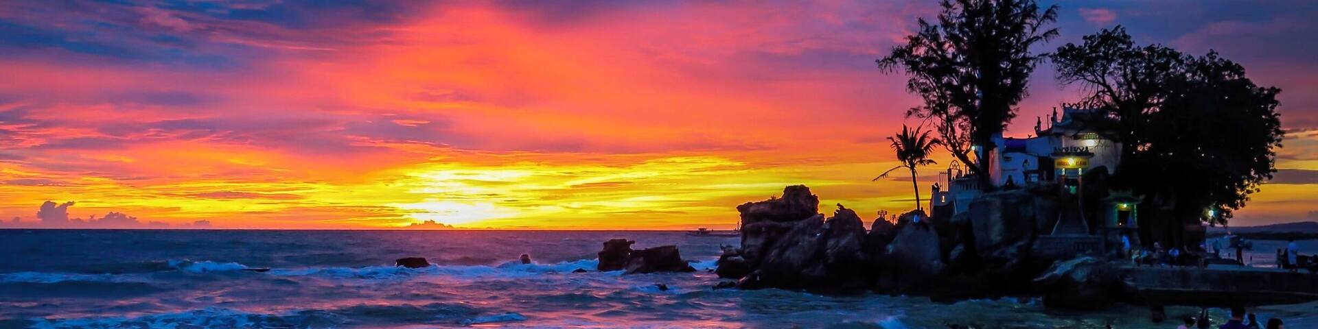 Atardecer sobre una playa con formaciones rocosas y un edificio a la derecha.