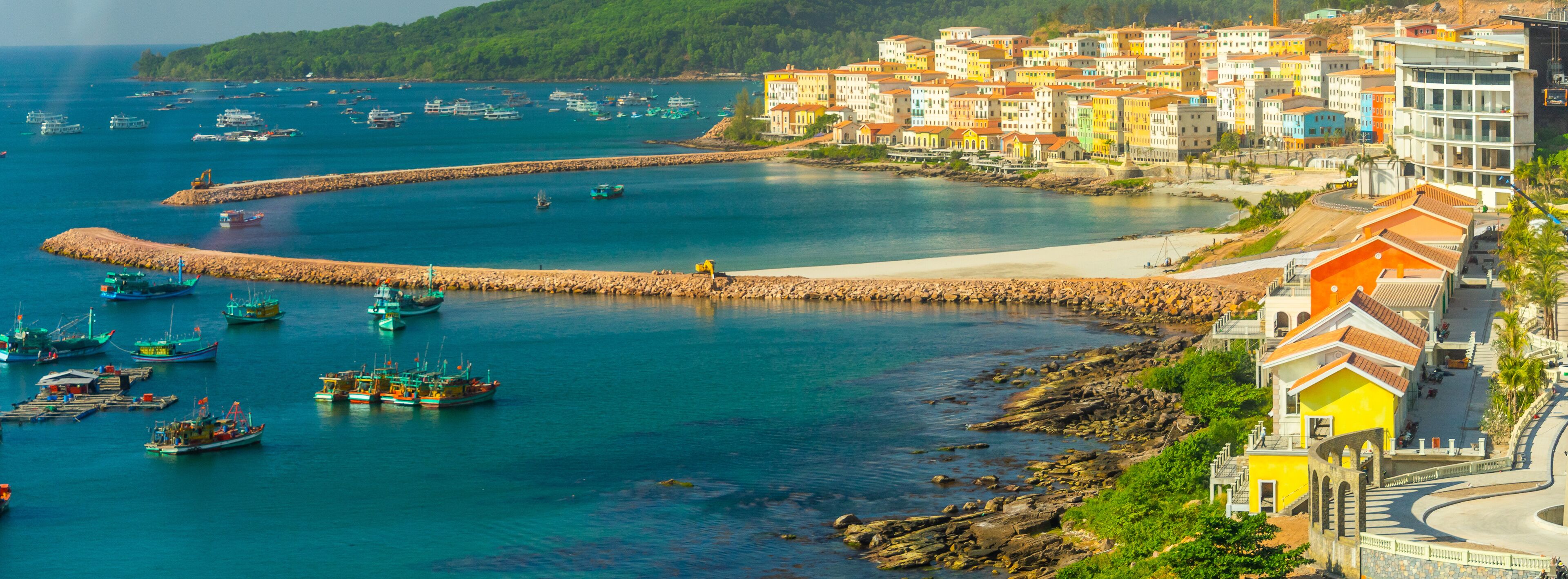 A coastal town with colorful buildings, a rocky breakwater, and boats in the water.