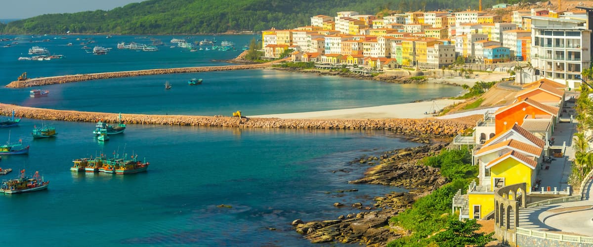 A coastal town with colorful buildings, a rocky breakwater, and boats in the water.
