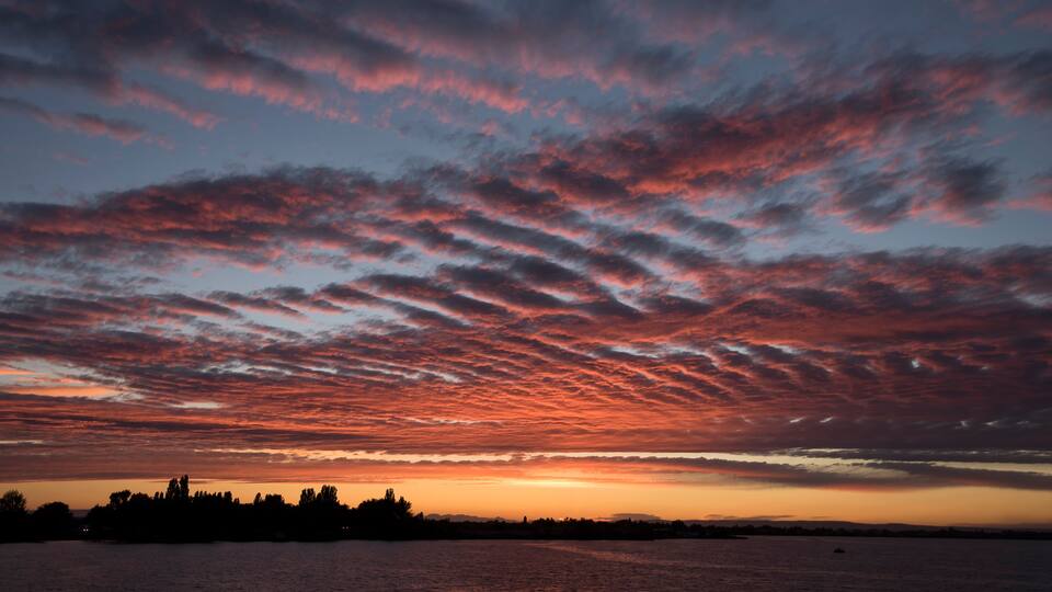 A sunset over a body of water with a silhouette of trees and a distant shoreline.