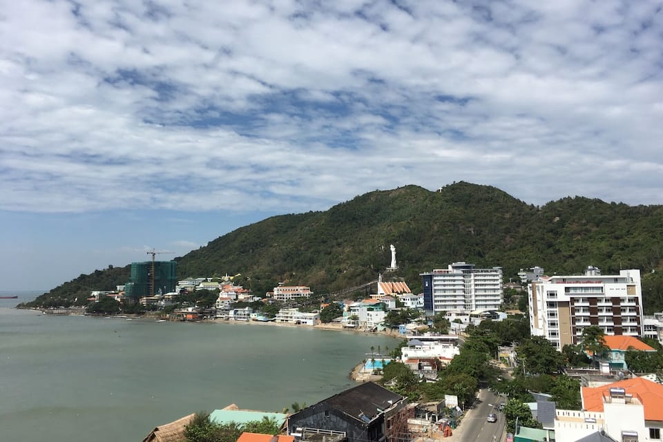 A coastal town with a mountain in the background, a statue, and a body of water.