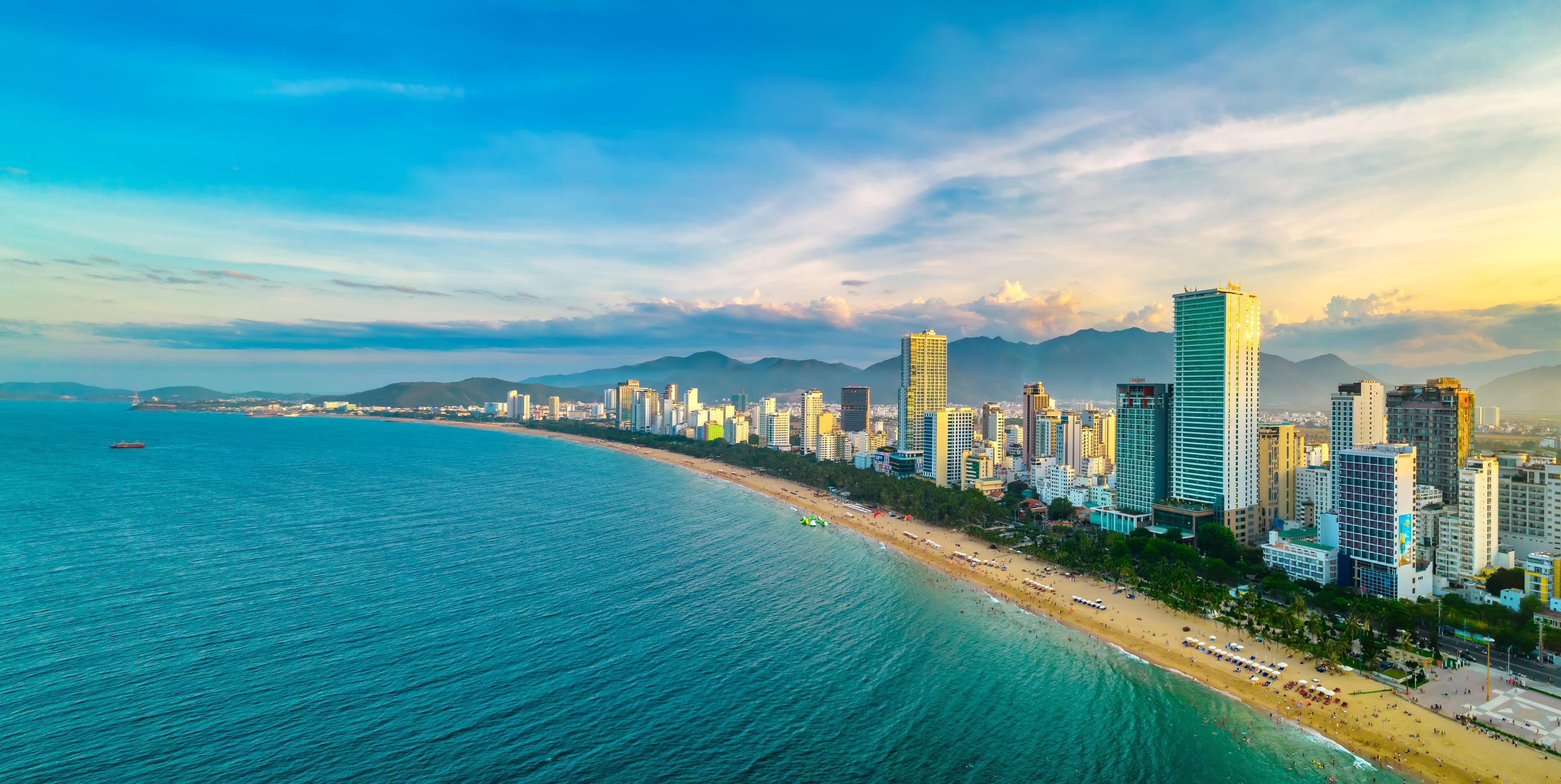 A coastal cityscape with a beach, high-rise buildings, and mountains in the background.