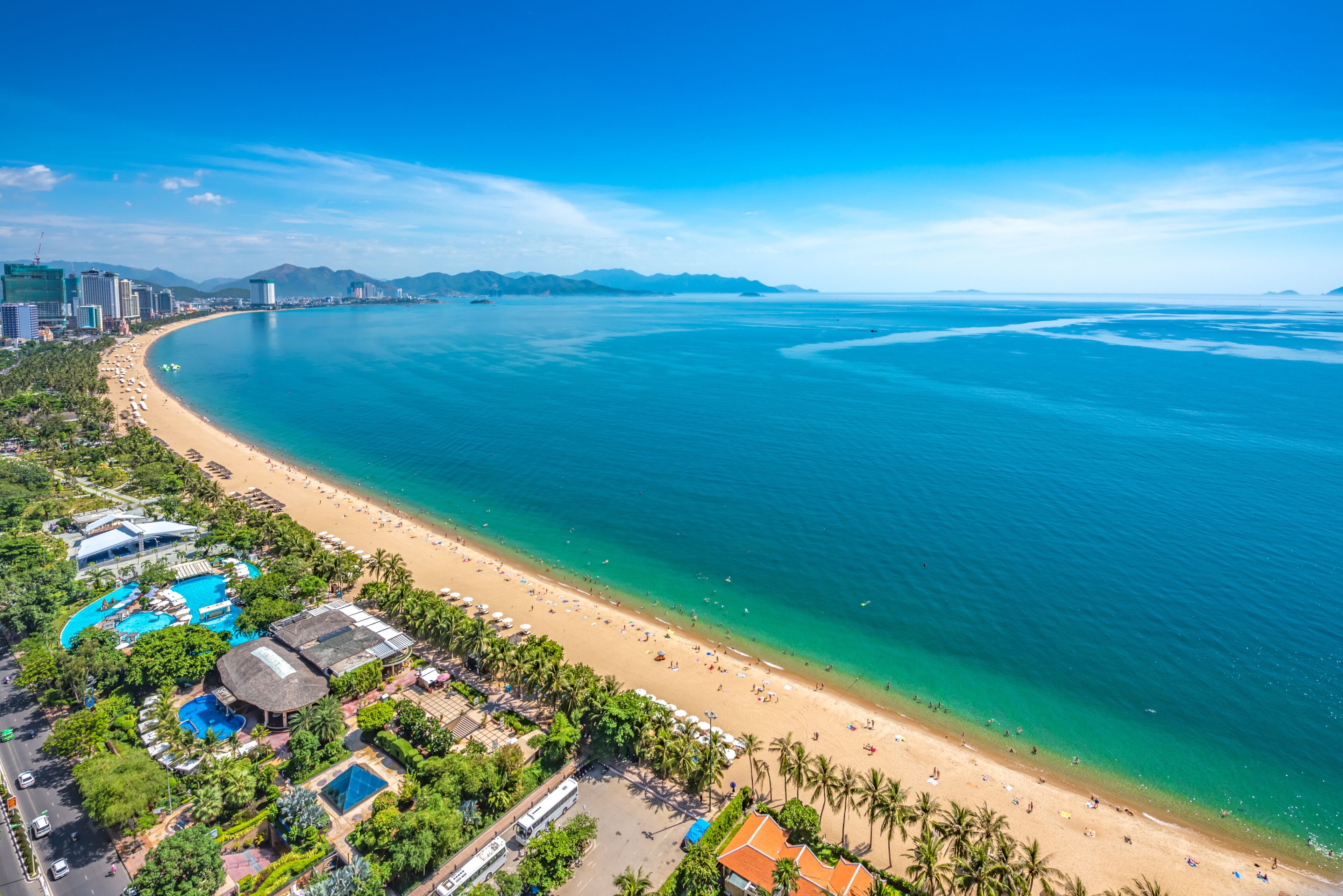 Um resort costeiro com praia, piscinas e mar azul cristalino.
