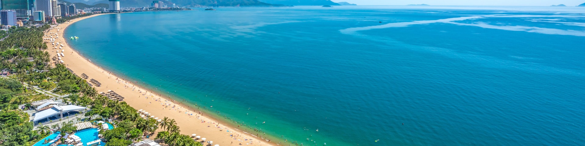 Um resort costeiro com praia, piscinas e mar azul cristalino.