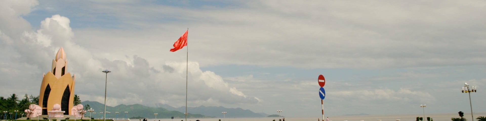 A road with traffic signs, a large lotus-shaped monument, and a flagpole with a flag.