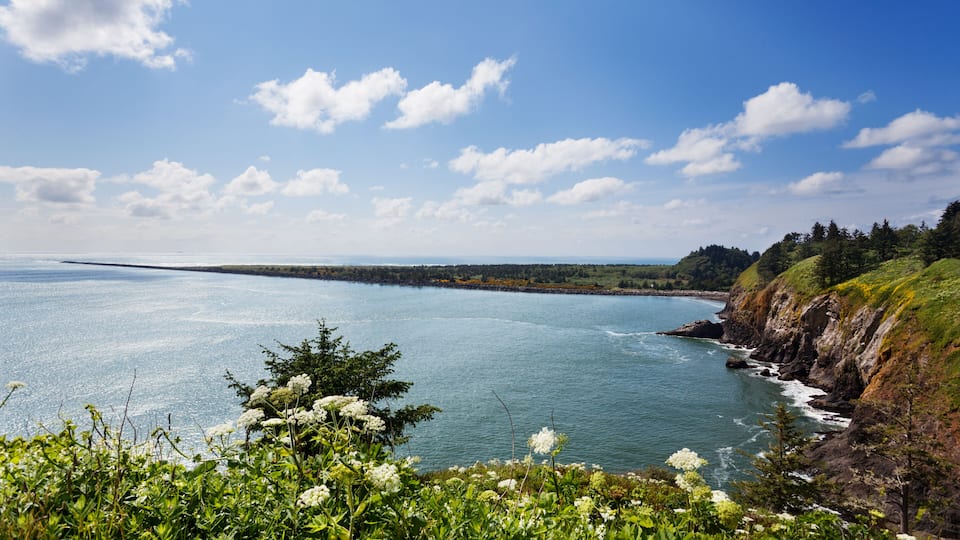 A coastal landscape with a clear sky, a calm sea, and a rocky shoreline.