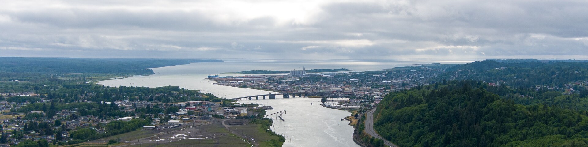 A river flowing through a city with a bridge, surrounded by hills and greenery.