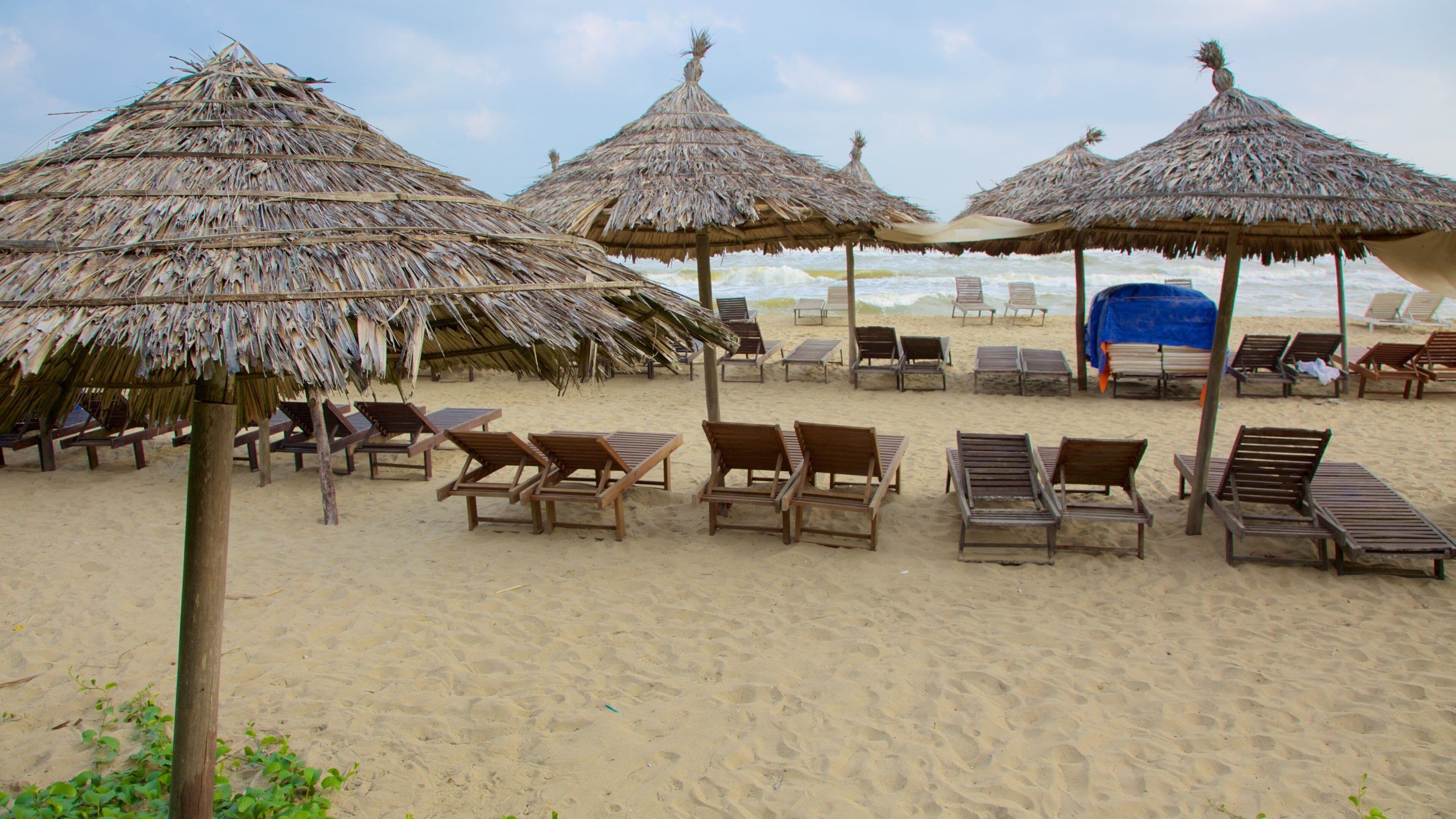 Una playa con sombrillas de paja y sillones de madera.