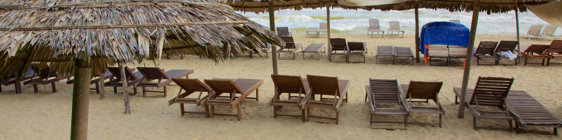 Una playa con sombrillas de paja y sillones de madera.