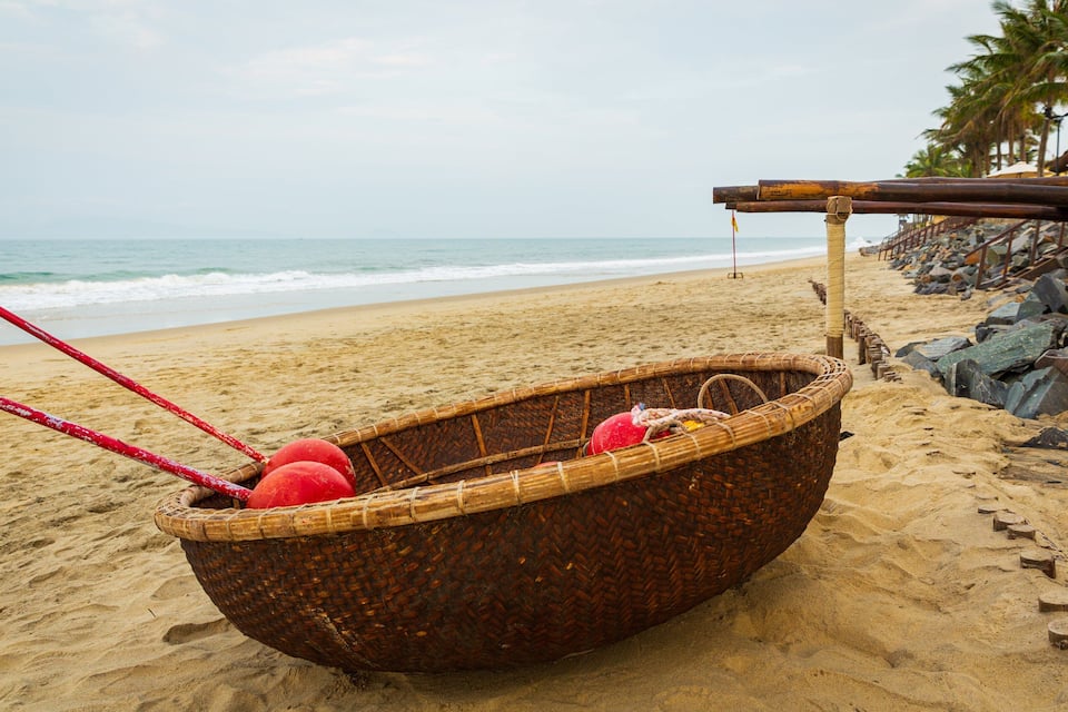 Una embarcación tejida tradicional con remos rojos sobre una playa arenosa.