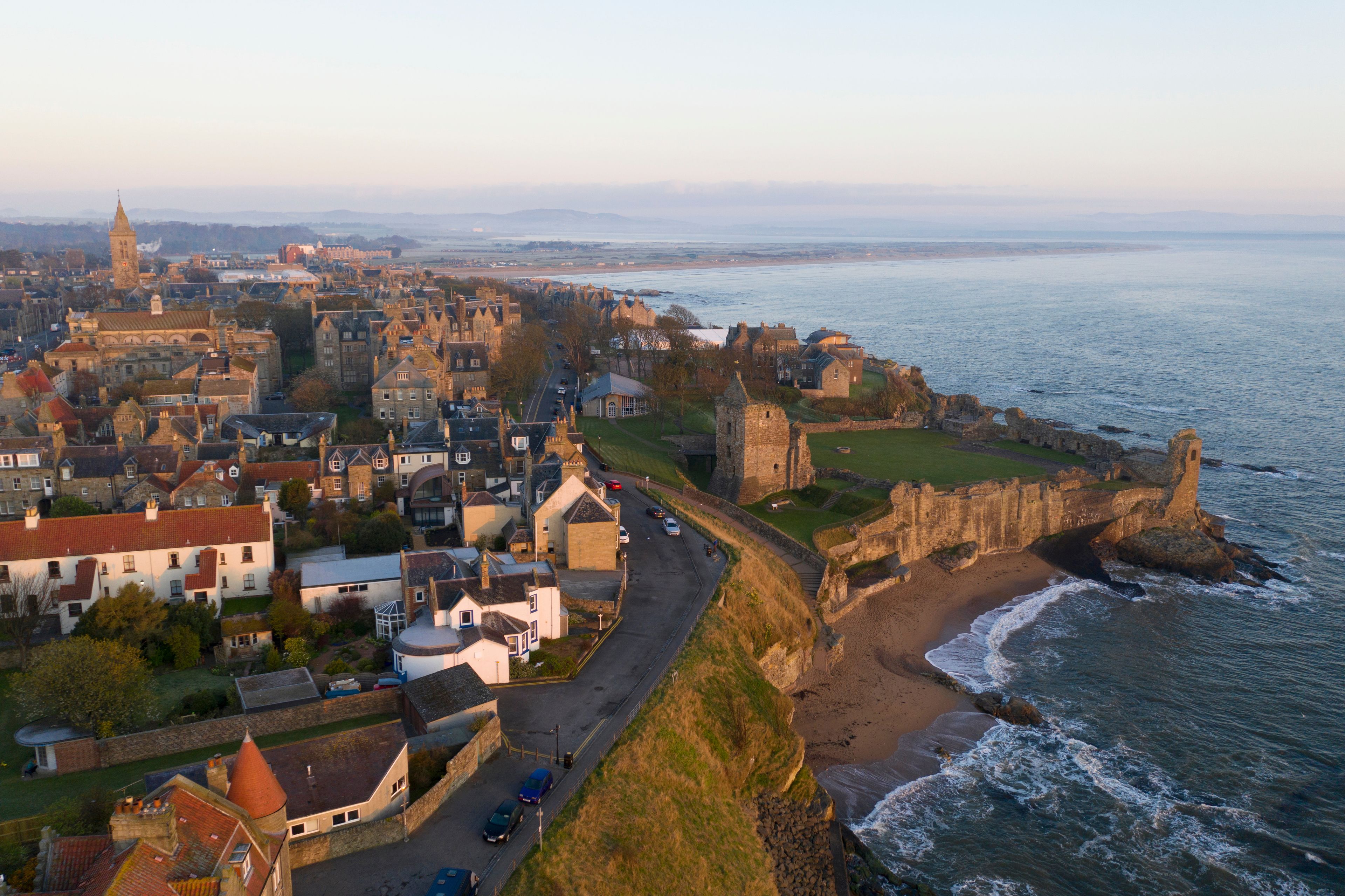 A coastal town with historic buildings, a prominent tower, and a fortified structure by the sea.
