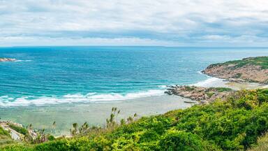 A coastal landscape with a clear blue sea, green hills, and rocky outcrops.