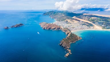 Vista aérea de uma cidade costeira com praia, formações rochosas e montanhas ao fundo.