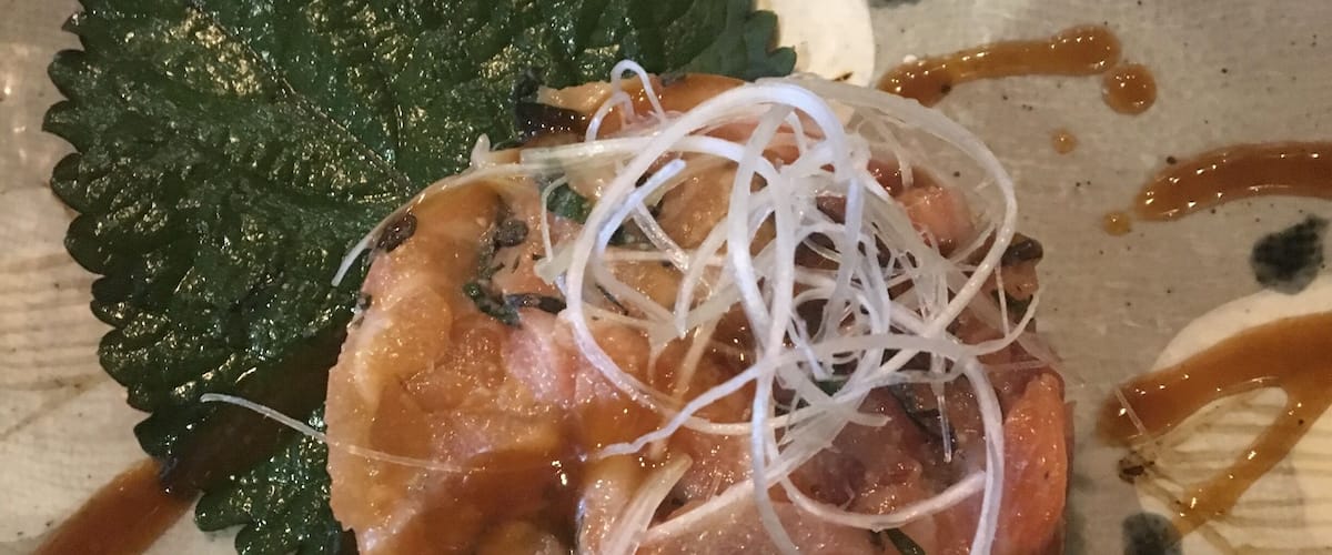 A plate with a seafood dish, garnished with a leaf and drizzled with sauce.