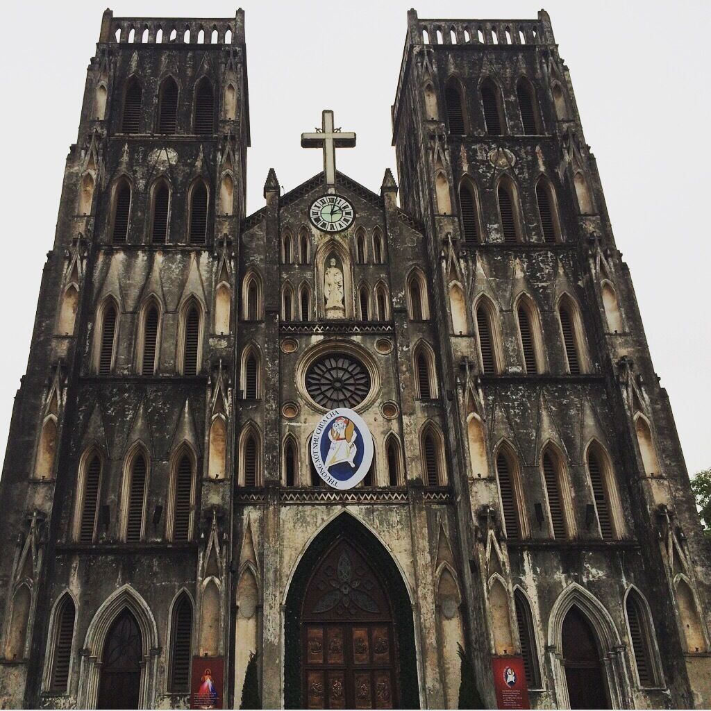 A Gothic-style church with twin towers, a large clock, and a cross at the top.