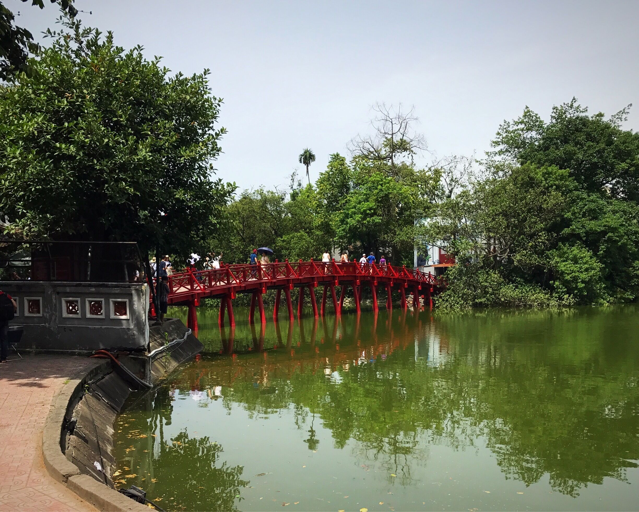 Un pont rouge enjambe une rivière paisible, le tout étant entouré d’une végétation luxuriante.