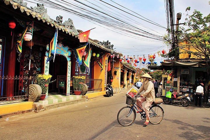 A traditional street with colorful buildings, a person riding a bicycle, and a market scene.