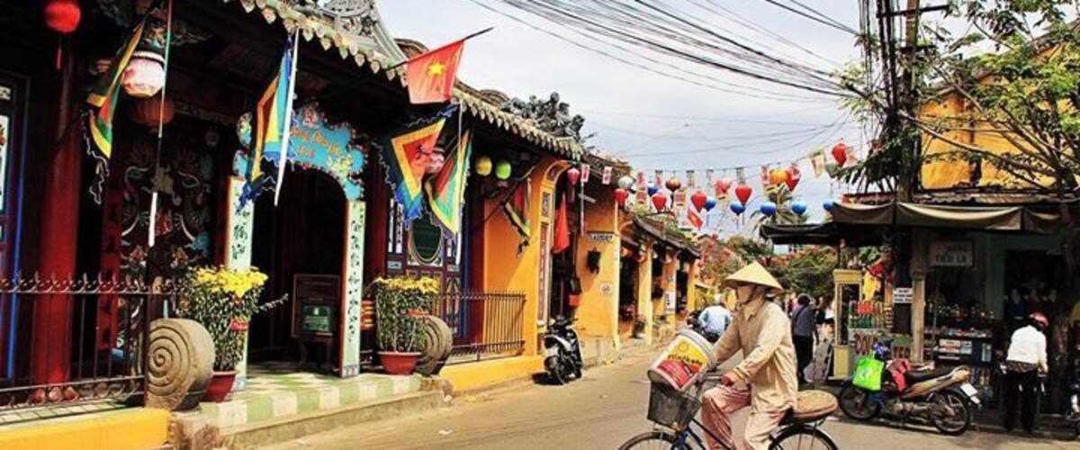 A traditional street with colorful buildings, a person riding a bicycle, and a market scene.