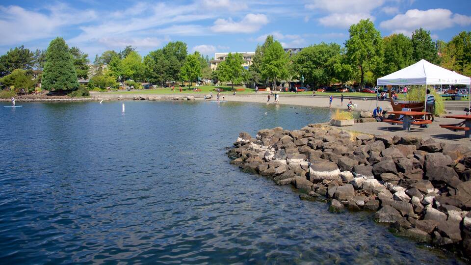 A calm lake with a rocky shoreline, picnic tables, and a white tent in a park.
