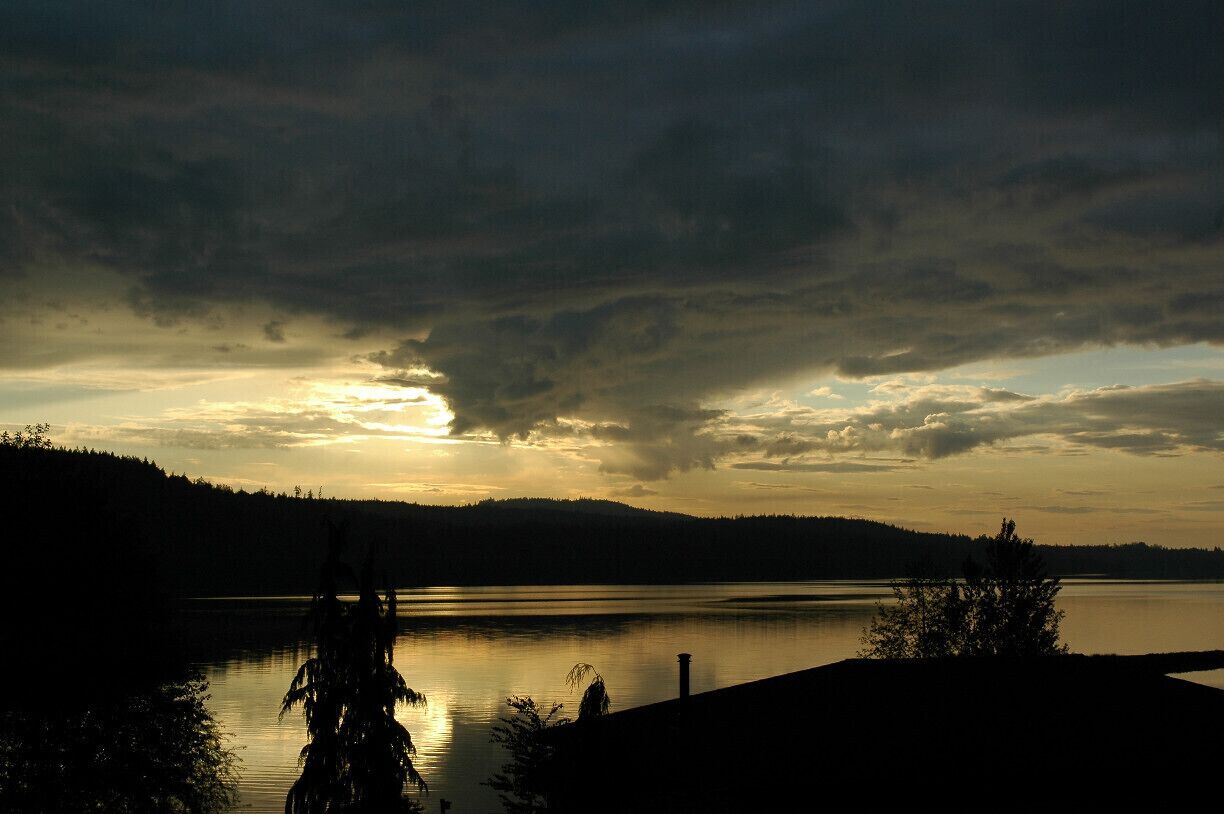 A lake at sunset with a forested shoreline and a cloudy sky.