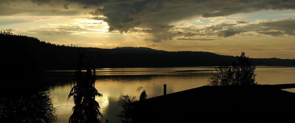 A lake at sunset with a forested shoreline and a cloudy sky.