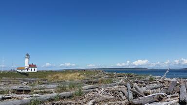 A lighthouse, rocky shoreline, and distant mountains under a clear sky.