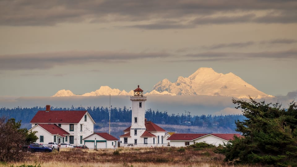 A lighthouse, a white house, and a mountain range.