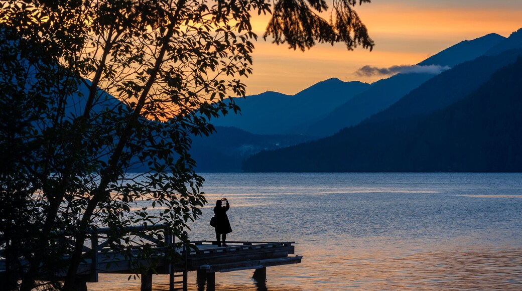 Woman Photographing a Dramatic Sunset on Lake Crescent, Washington. Using an cell phone a woman captures a beautiful sunset over the Olympic Mountains while standing on a pier at lake Crescent Lodge.