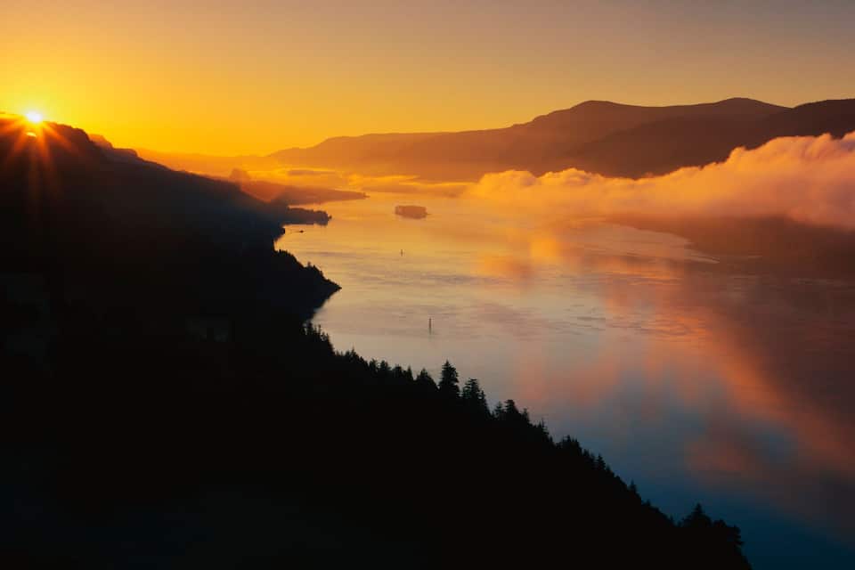 A sunset over a calm lake with mountains in the background.