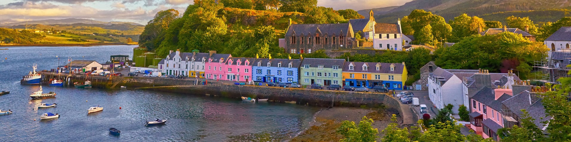 A coastal town with colorful houses, a pier, boats, and a hill with a church.