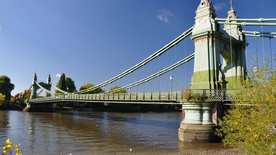 A suspension bridge with green towers and cables over a river.