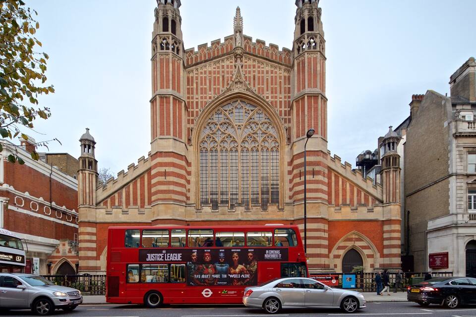 A red double-decker bus in front of a Gothic-style church with a large arched window and two towers.