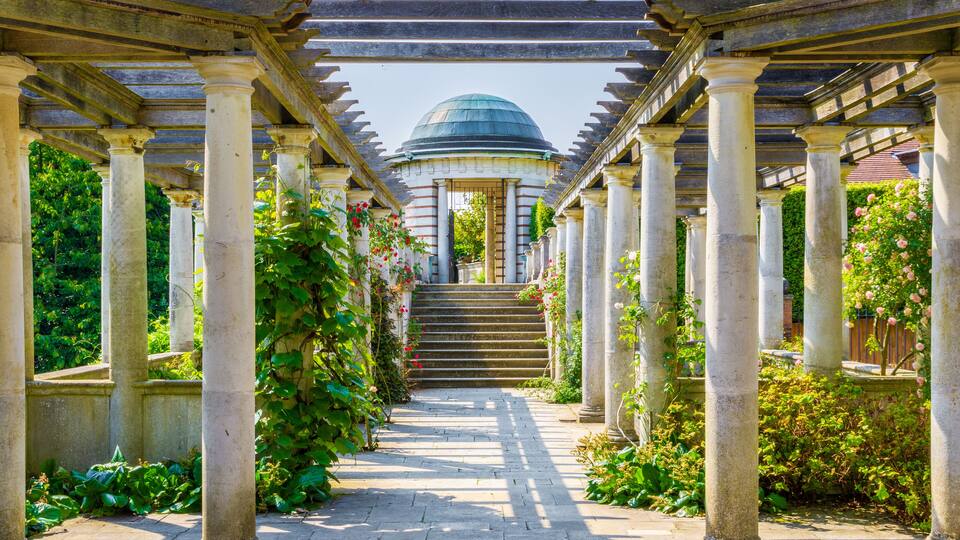 A classical garden with a central dome, stone columns, and a paved pathway.
