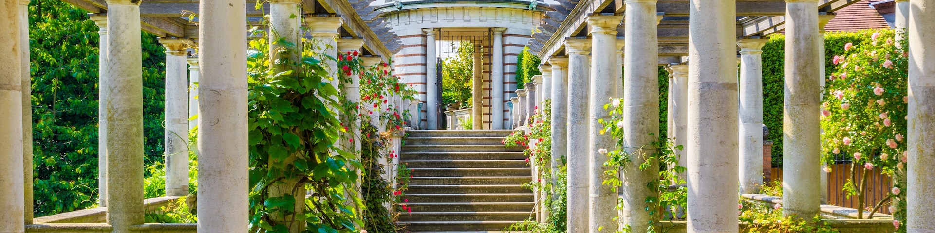 Un jardín clásico con una cúpula central, columnas de piedra y un camino empedrado.