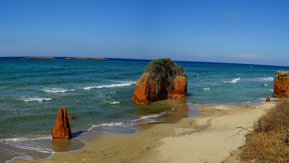 A beach with clear blue waters, rocky formations, and a distant island.