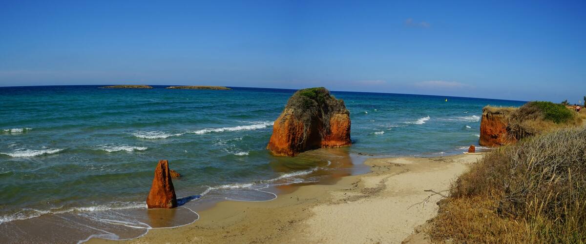 A beach with clear blue waters, rocky formations, and a distant island.