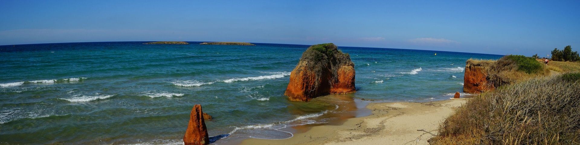 A beach with clear blue waters, rocky formations, and a distant island.