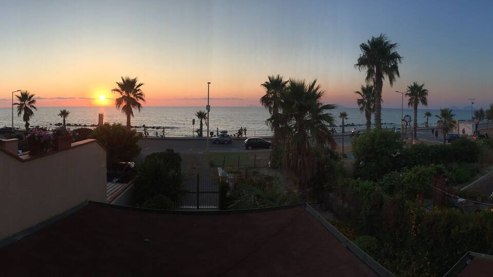 A sunset over a coastal area with palm trees and a road with cars.