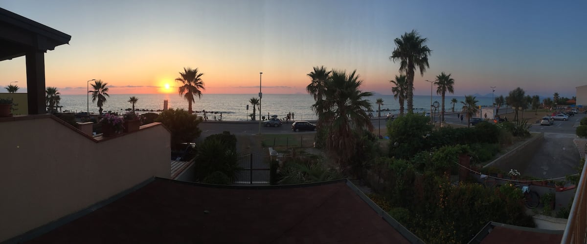 A sunset over a coastal area with palm trees and a road with cars.