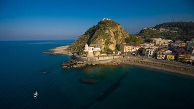A coastal town with a prominent hill, a lighthouse, and a clear blue sea.