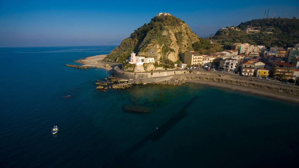 A coastal town with a prominent hill, a lighthouse, and a clear blue sea.