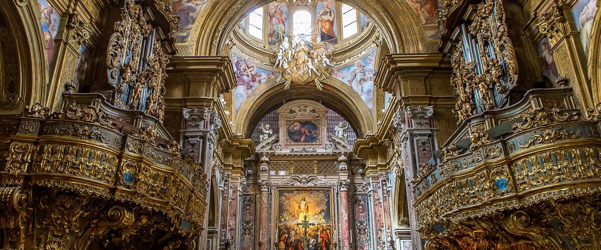 An ornate church interior with intricate gold detailing, a large chandelier, and a central altar.
