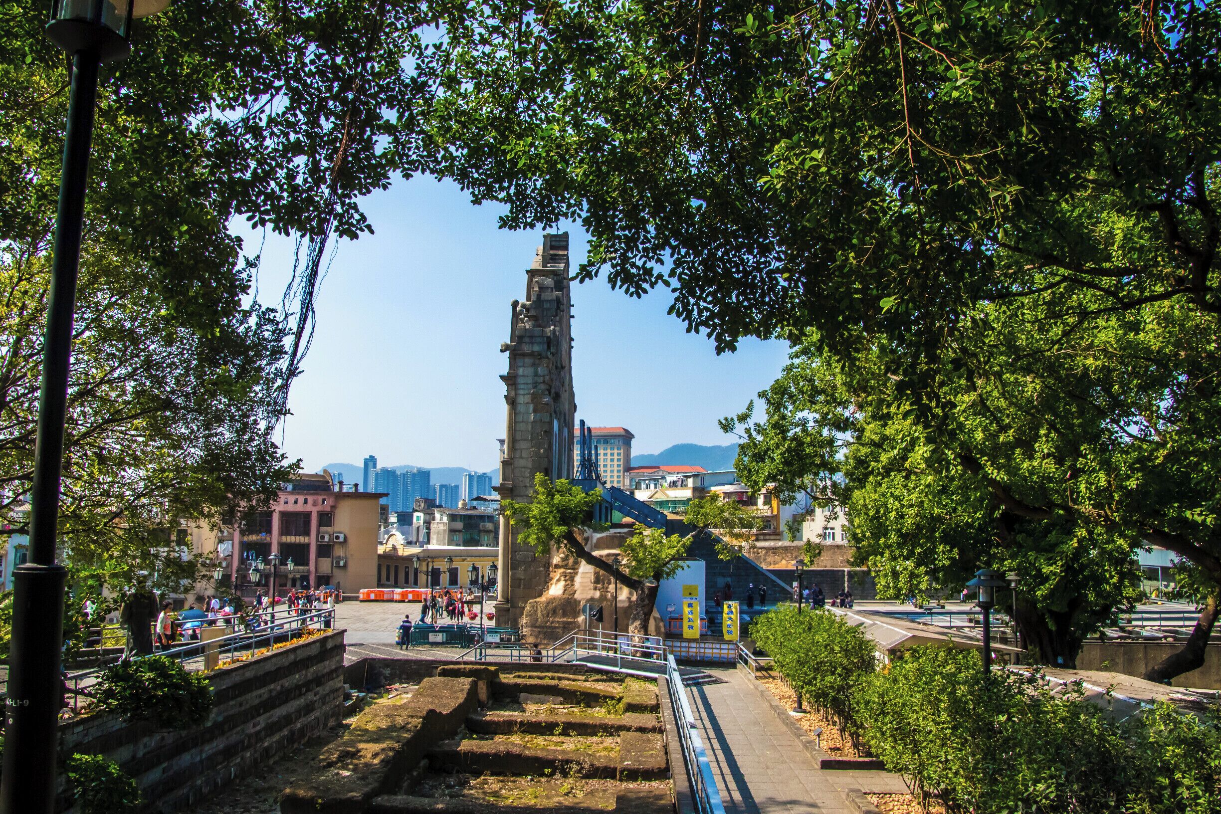 Una torre de piedra histórica rodeada de árboles, con edificios modernos al fondo.