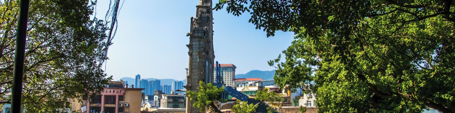 Una torre de piedra histórica rodeada de árboles, con edificios modernos al fondo.